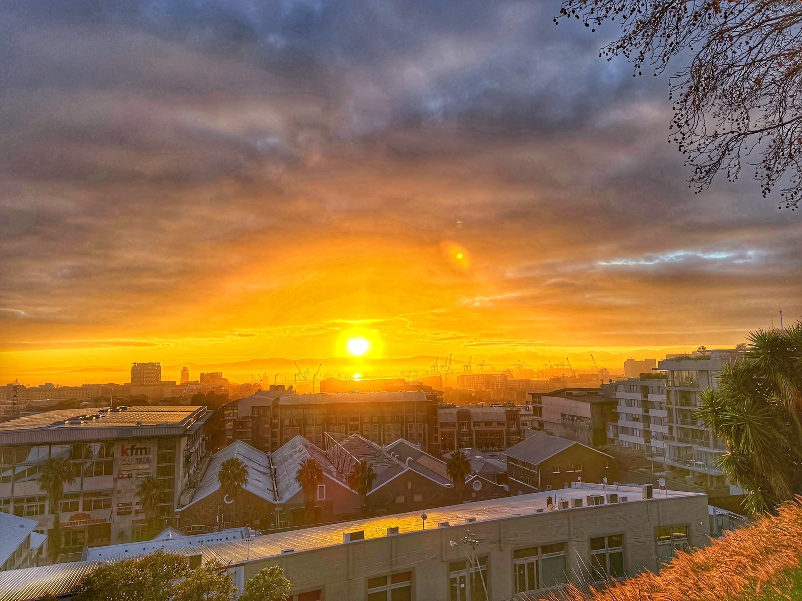 The sun rising low over Table Bay harbour, its light flooding a broken cloud ceiling and reflecting off the metal rooftops of Cape Town's city bowl.